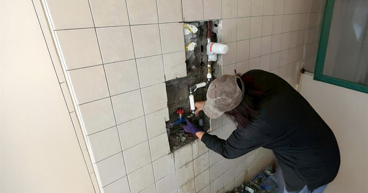 浴室の壁内で給排水管の修理を行う伊藤設備総業の職人